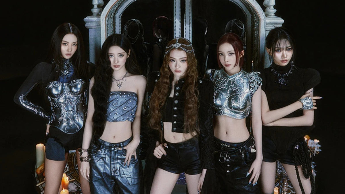 Five women posing together in gothic, high-fashion outfits with metallic silver and black elements, set against a dark background with a large ornate gothic arch and candles.