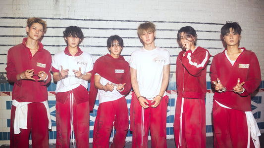 Six young men standing together in matching red and white tracksuits against a white brick wall background.