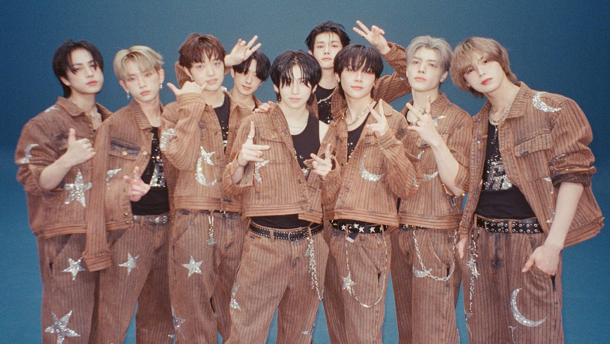 Nine young men posing together in matching brown corduroy tracksuits with white star and moon appliques, set against a solid blue studio background.
