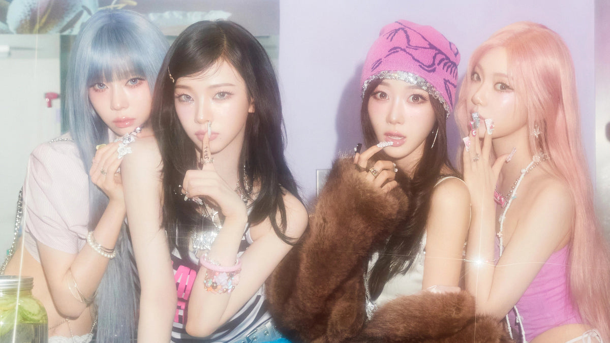 Four women posing together in a brightly lit room with pastel lighting, styled with colorful clothing and accessories. A mannequin head with long brown hair is visible in the bottom right corner.