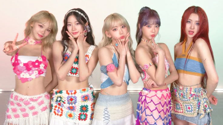 Five women posing together in colorful crochet and knit mini outfits with fringe details, set against a plain light background.