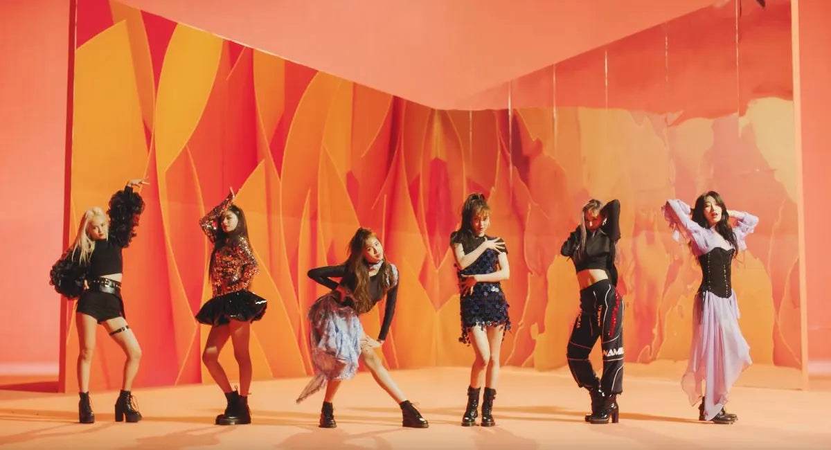 Six women posing in coordinated outfits against a stylized orange and pink abstract backdrop.